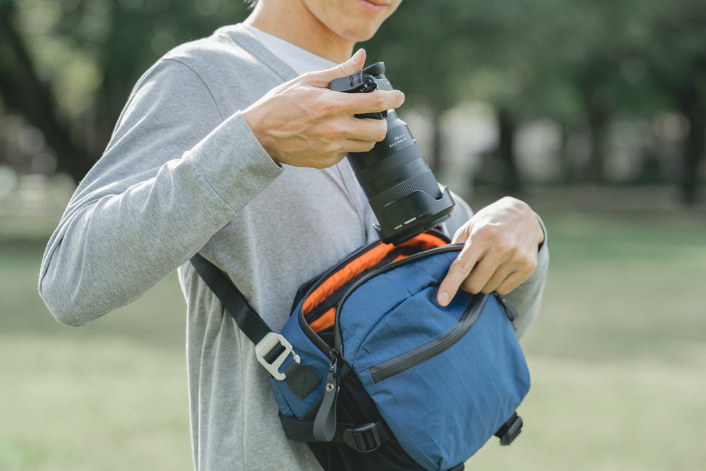 Man in grey putting a camera into X-Pac Blue crossbody camera bag