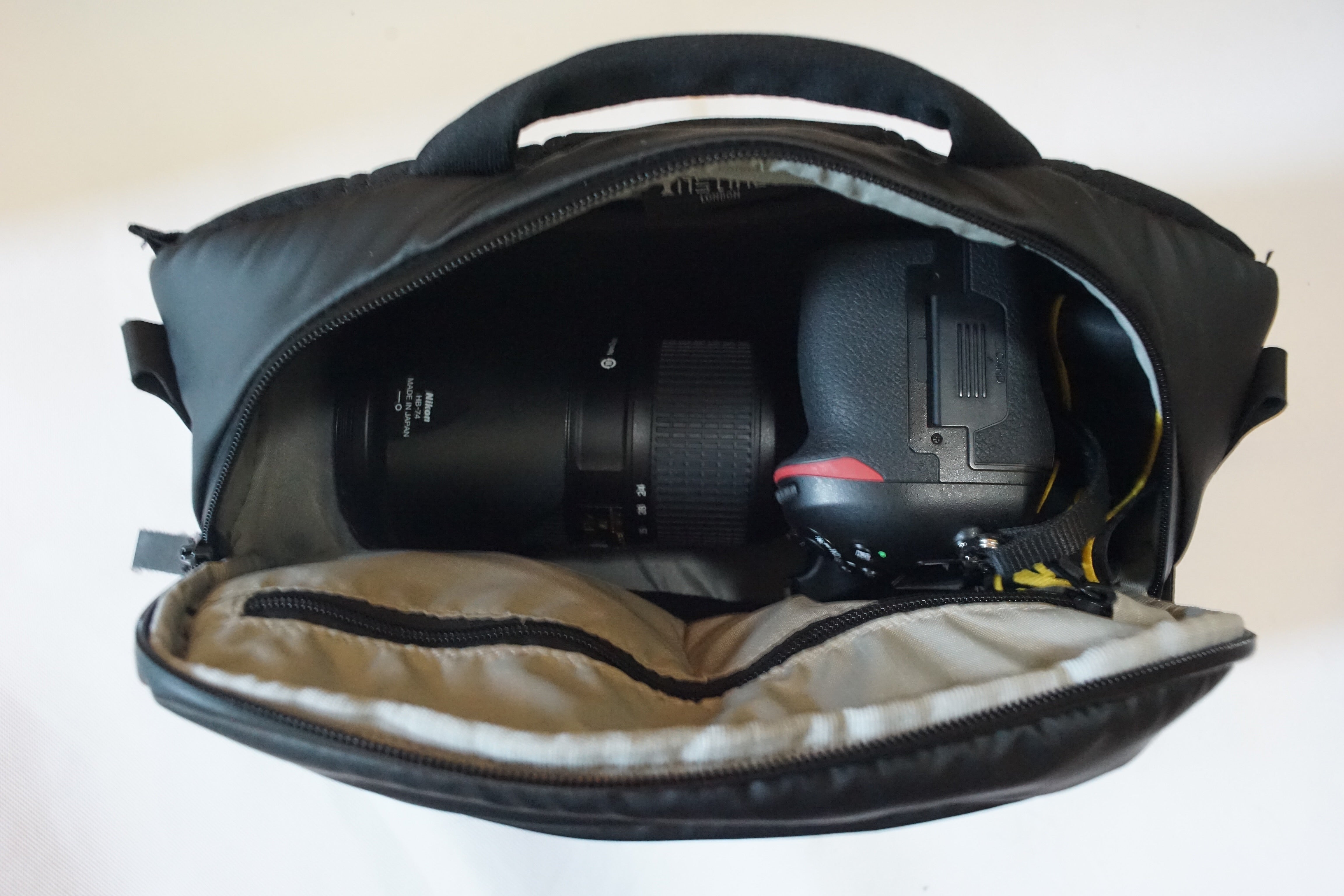 Nikon camera with lens inside black camera sling bag with grey lining